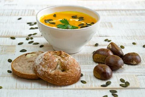 Low angle view of organic pumpkin soup in a white bowl framed by chestnuts and Stock Photos
