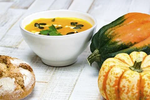 Low angle view of organic pumpkin soup in a white bowl framed by pumpkins and Stock Photos