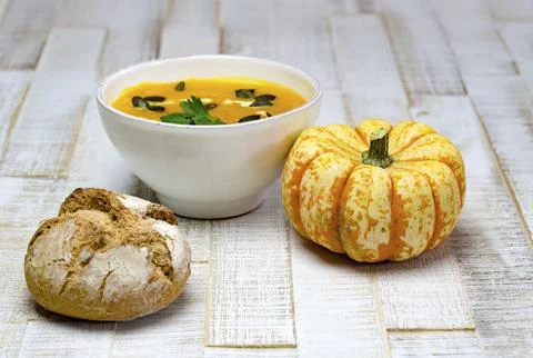 Low angle view of organic pumpkin soup in a white bowl framed by pumpkin and Stock Photos