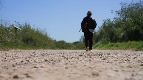 Low angle view of a person walking away along a gravel road in a rural area Stock Footage 334713803