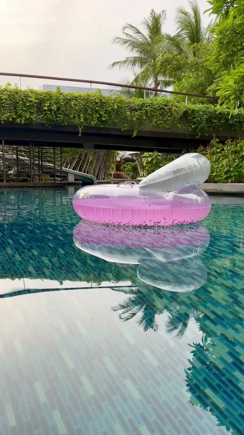 Low-angle view of a pink inflatable chair peacefully floating across a luxury Vídeos de archivo 345888816