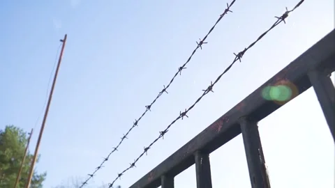 Low angle view POV of wire fence above metal doors protective layer spikes Stock Footage 254186582
