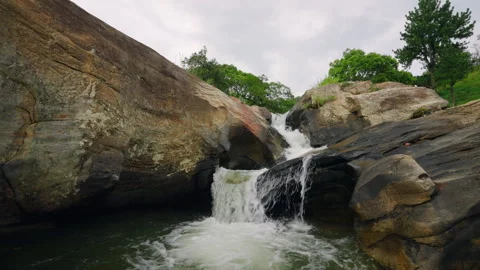 Low angle view of powerful waterfall cascading down rocky terrain, rich trees Stock Footage 275117427