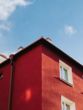 Low angle view of a red building corner with white windows, set against a blue Stock Photos