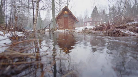 Low angle view of river floodwaters encroaching on tiny wooden cabin in woods Video stock 298146282