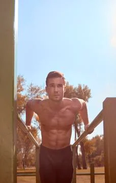 Low angle view of shirtless man exercising on parallel bars against sky at park Stock Photos