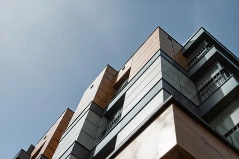 Low angle view shows modern apartment building facade with wood panels and Stock Photos