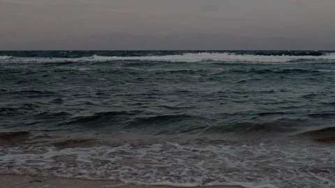 Low-angle view of small waves breaking onto sandy shore under overcast sky Stockbeeldmateriaal 347304876