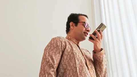 Low-angle view of smiling Indian businessman making a mobile call near window Stock Footage 325967472
