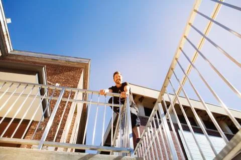 Low angle view of smiling man standing on building railing against clear blue Fotos de archivo
