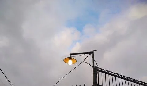 Low angle View of the street light bulb turned on against a cloudy gray sky Stock Photos