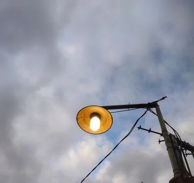 Low angle View of the street light bulb turned on against a cloudy gray sky Stock Photos