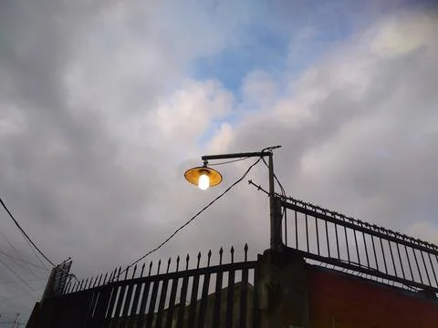 Low angle View of the street light bulb turned on against a cloudy gray sky Stock Photos