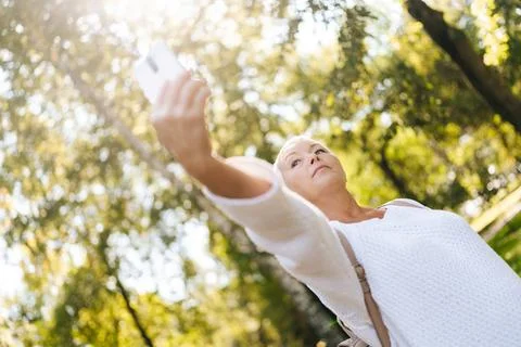 Low-angle view of stylish gray-haired senior woman taking selfie using mobile Stock Photos