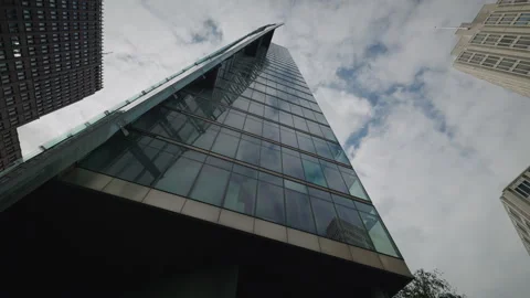 Low-angle view of a tall glass skyscraper with a curved tapered top, flanked by Stock Footage 346240405