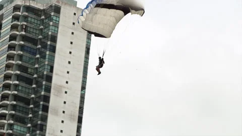 Low-Angle View Tracking A Man As He Parachutes Past A Modern Highrise Building - Stockbeeldmateriaal 196899484