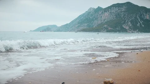 Low angle view tracking shot of a sandy sea shore with waves and sea foam Видео 103990410