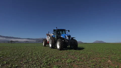 Low angle view tracks tractor and sprayer on crop field under blue sky Stock Footage 301062778