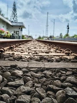Low angle view of train tracks with gravel stones and station background Stock Photos