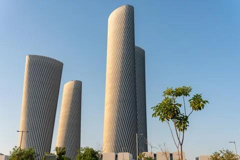 Low-angle view of the twisted Lusail Plaza Towers with surrounding trees. Photos