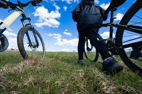 Low-angle view of two individuals pushing their mountain bikes across a grass 스톡 사진