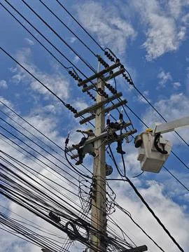 Low angle view of two lineman electricians sitting on utility riser pole. Stock Photos