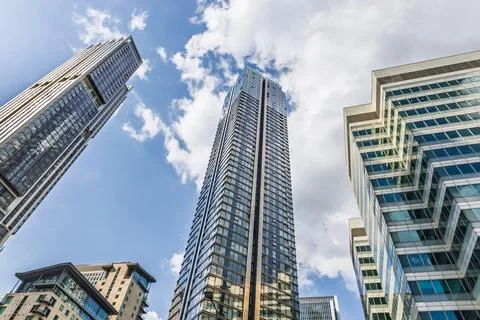 Low angle view of ultra modern glass skyscraper soaring into blue sky with Stock Photos