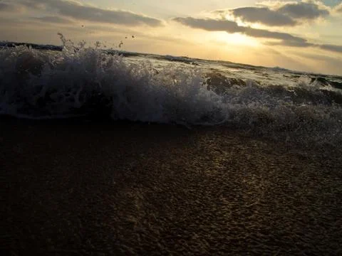 Low angle view of a wave splashing on shore under a cloudy sky at sunset 写真素材