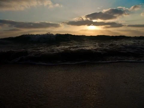 Low angle view of a wave splashing on shore under a cloudy sky at sunset 写真素材