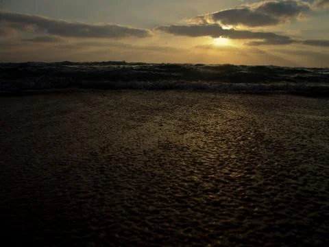 Low angle view of a wave splashing on shore under a cloudy sky at sunset Foto stock
