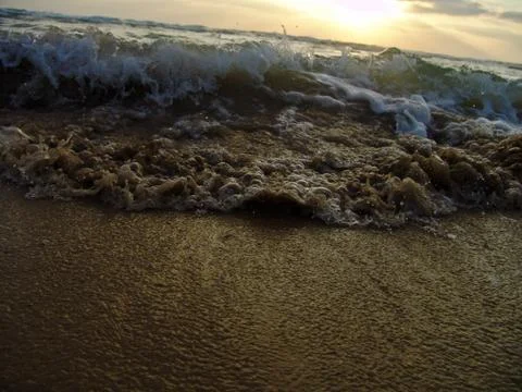 Low angle view of a wave splashing on shore under a cloudy sky at sunset 写真素材