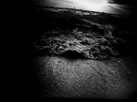 Low angle view of a wave splashing on shore under a cloudy sky at sunset Foto stock