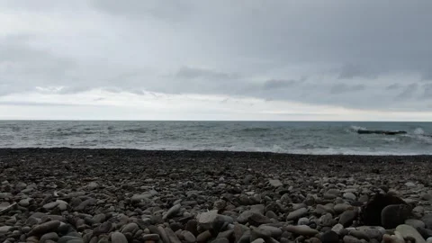 Low angle view of waves on pebble beach under cloudy sky, D-Log footage Vidéo 321017985