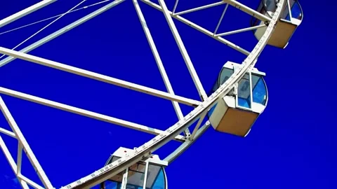 Low angle view of white ferris wheel gondolas rotating against vivid blue s.. Stock Footage 348289719