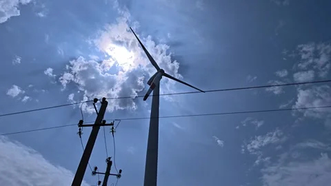 Low angle view of a wind turbine spinning and a power pole silhouetted agai.. Video stock 342925645