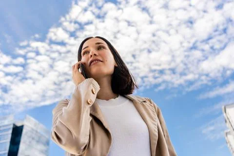 Low-angle view of a woman talking on her cell phone as she looks ahead. Stock Photos