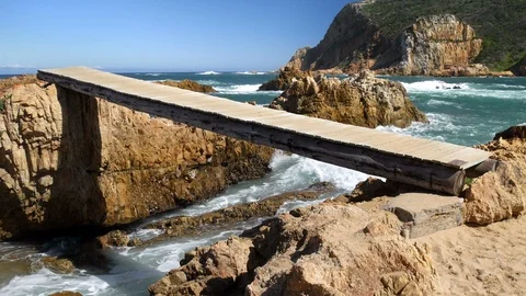 Low angle view of wooden bridge across rocks gap with ocean waves 库存影片 107566226