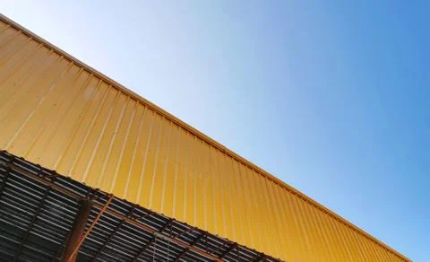 Low Angle View of Yellow Corrugated Roof Exterior Against Blue Sky Foto stock