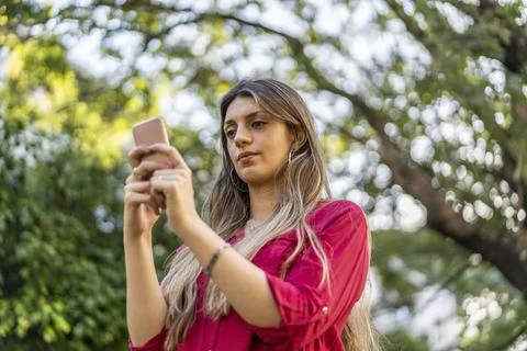 Low angle view of young blond woman using smartphone outdoors.  Modern tech.. Stock Photos