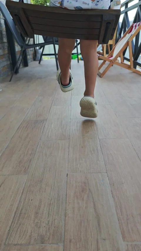 Low angle view of young child jumping on wooden terrace swing, embodying 库存影片 314522640