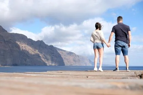 Low angle view of a young couple holding hands with cliffs, cloudy sky and th Stock Photos