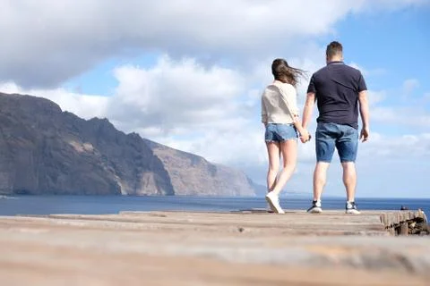 Low angle view of a young couple holding hands with cliffs, cloudy sky and th Stock Photos