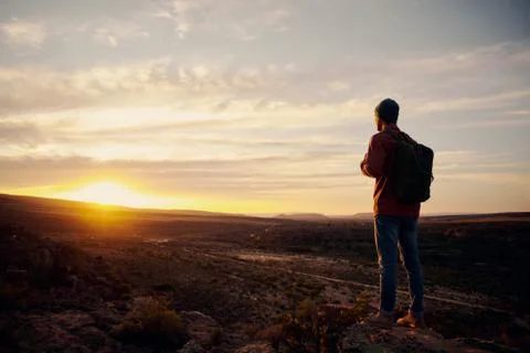 Low angle view of young male hiker with backpack standing on mountain top while Stock Photos