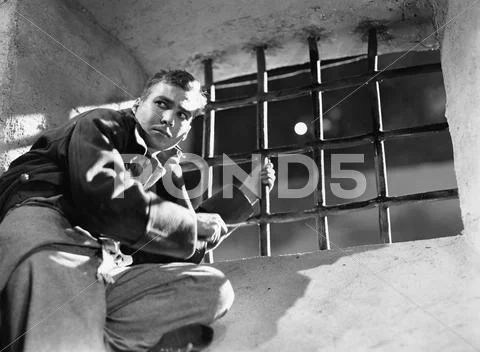 Low angle view of a young man trying to escape from a prison cell Stock Photos