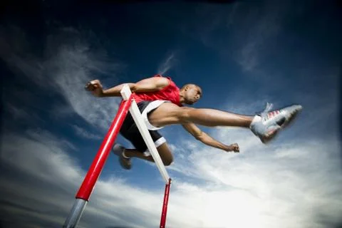 Low angle view of a young man jumping over a hurdle in a race Foto stock