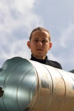 Low angle view of a young working man holding a metal or aluminium duct Foto stock