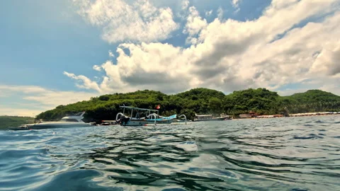 Low angle water level view of anchored boats near a tropical island Видео 333097683