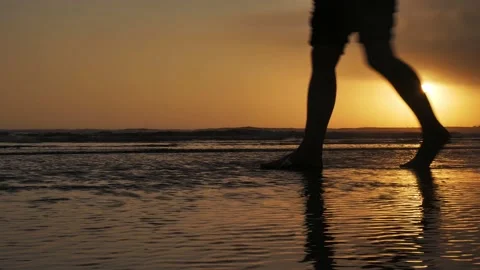 Low angle of waves on beach and legs of person walking by during sunset Stock Footage 143425283
