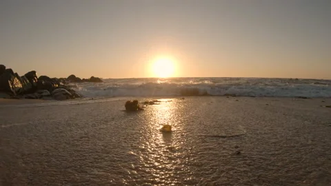 Low angle waves washing over shoreline of sandy beach at sunset in summer Stock Footage 139571248