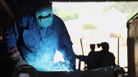 Low angle welder welding at workbench, worker walks past in background Stock Footage 307482811